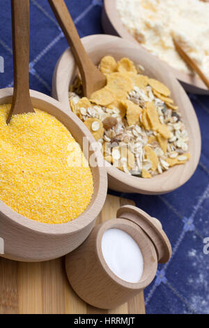 Salt in a small wooden bowl placed on the wooden plate with cereals and corn flour Stock Photo