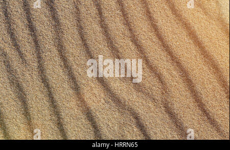 Texture of yellow sand. Beach sand patterns in warm evening sunlight. Straight rows of sand on beach. Close up of sand. Beautiful sand background for  Stock Photo