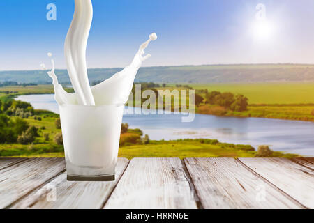 Milk pouring in glass. Close up of milk splash. Milk in glass on wood table. Glass with white milk on sunrise background. Colorful beverage background Stock Photo