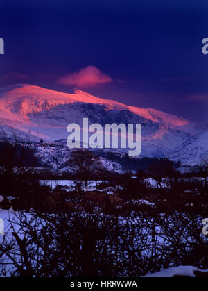 Pyramidal summit of Snowdon 3560ft (1085m), North Wales, seen from the NW with Garnedd Ugain to L, covered in snow & lit by setting sun. Stock Photo