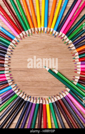 color pencils arranged in a circle on wooden background, top view. Brown table. Two green pencils stand out of other pencils. Art and design. Artist.  Stock Photo