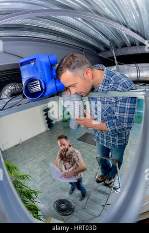 Man on ladder holding pipes in celing Stock Photo