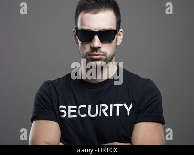 Dramatic portrait of tough macho security guard man with crossed arms over dark gray studio background Stock Photo