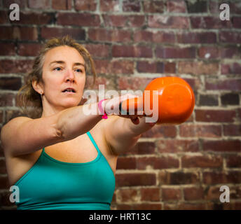 A woman in her early 40's swinging a kettlebell while working out. Stock Photo