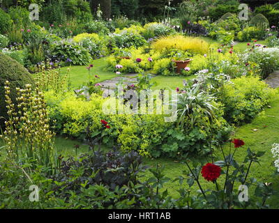 Chenies Manor Sunken garden in summertime with dahlias and lush green foliage plants around the ornamental pond and herbaceous borders; grassy paths. Stock Photo