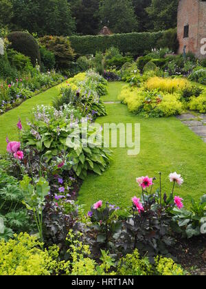 Portrait view of Chenies Manor sunken garden, Buckinghamshire. Lush green growth with colourful dahlias, hosta leaves, herbaceous plants and pavilion. Stock Photo
