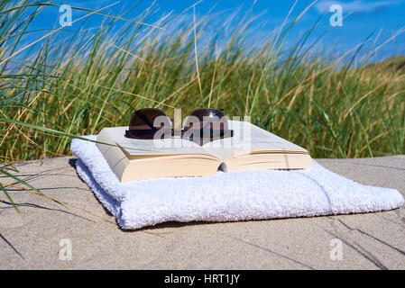 Book on the beach with sunglasses an weed in the background Stock Photo