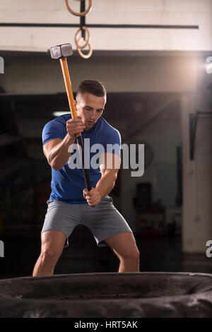 Sledgehammer Tire Hits young muscular man workout at gym with hammer and tractor tire Stock Photo