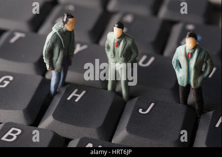 Miniature male figures standing on computer keyboard Stock Photo