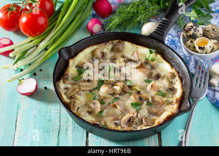 Omelette from quail eggs with ham and bacon in a cast iron frying pan on a wooden table. The concept of healthy nutrition and diet. Stock Photo