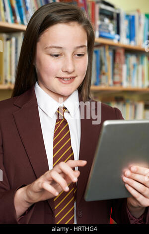 Girl Wearing School Uniform Using Digital Tablet In Library Stock Photo