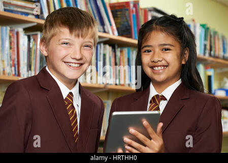 Portrait Of Pupils Wearing School Uniform Using Digital Tablet In Library Stock Photo