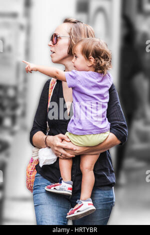 Mum walks on the street and carries young child that indicates something she noticed Stock Photo