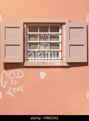 Wooden window in pink house wall with graffiti god is love. Simple wood window Stock Photo