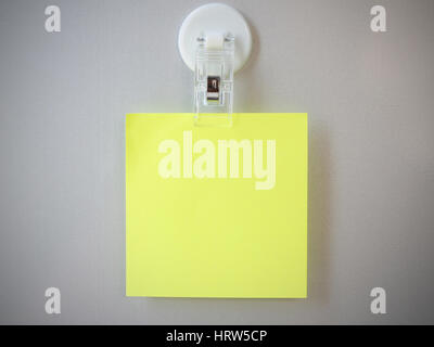 Yellow post it clip by clip magnet on gray refrigerator background. Stock Photo