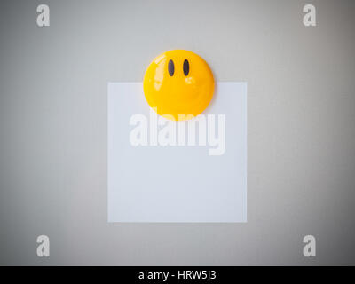 Yellow magnet paper clip on gray refrigerator background, abstract background. Stock Photo