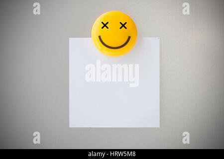 Plastic magnet paper clip on paper note on gray refrigerator background for input text. Stock Photo