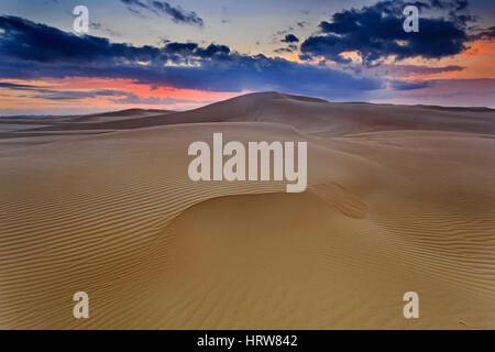 Colourful pink sunrise with dark clouds over untouched sand dunes of coastal area in Australia. Stripped pattern and structure on sand surface created Stock Photo