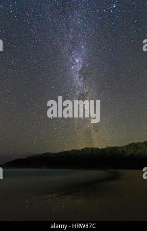 Milky way galaxy with southern cross constellation seen from sandy beach in Australia. Image contains noise and grains due to high ISO. Stock Photo