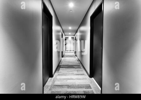 Symmetrical corridor in modern brand new hotel with room doors on sides and white walls lit by bright lights. No guests in sight. Stock Photo