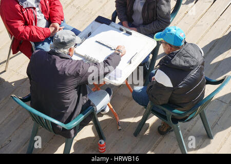 Barcelona, Spain - March 01, 2016: Four old men playing a game of domino at Barceloneta beach. Stock Photo