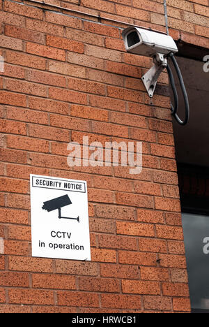 CCTV camera and warning notice on urban red brick wall Stock Photo
