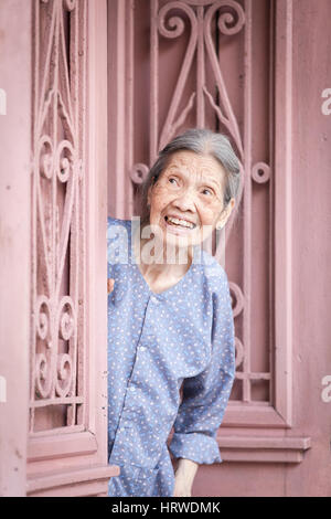Hanoi, Vietnam - April 26, 2014: Portrait of senior vietnamese woman looking out from the door on the street of Hanoi, Vietnam on April 26, 2014. Stock Photo