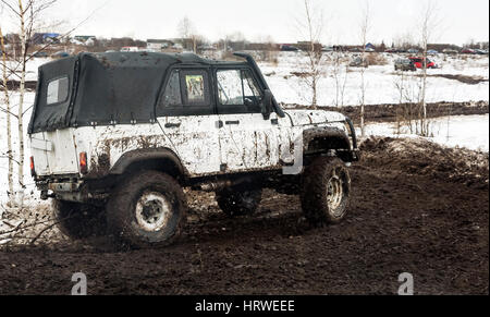 The car rides on a rough road in the winter, all stained with mud from the wheels. Stock Photo