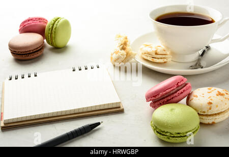 Cup of black tea with tasty varicolored macarons and notebook on a white background in light key. Copy space. Stock Photo