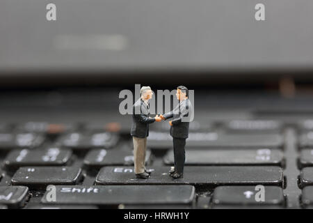 Selective focus of miniature businessman handshake on the button Enter button keyboard background as commitment concept. Stock Photo