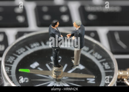 Selective focus of miniature businessman handshake on the compass background as commitment and teamwork concept. Stock Photo