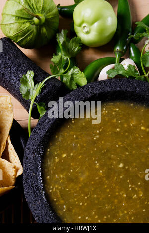 Stock image of mexican salsa verde on mortar and pestle with ingredients Stock Photo