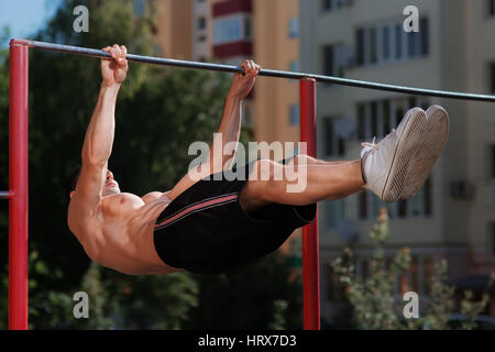 Fitness man doing stomach workouts on horizontal bar outdoors. Pulling on the bar. MAn in the black short and white sneakers. Abs. Healthy lifestyle.