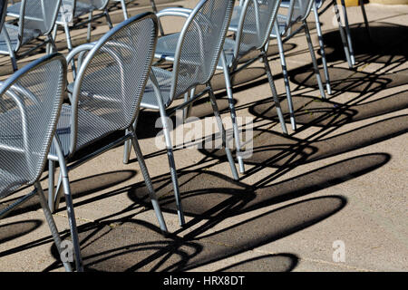 The shadow pattern on concrete, caused by low angle sunlight shining through metal mesh chairs. Stock Photo