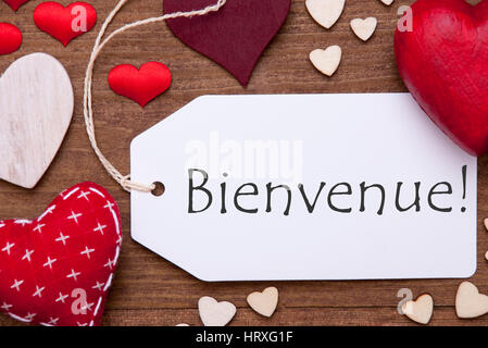 Label With French Text Bienvenue Means Welcome. Red Textile Hearts On Wooden Background. Flat Lay With Retro Or Vintage Style Stock Photo