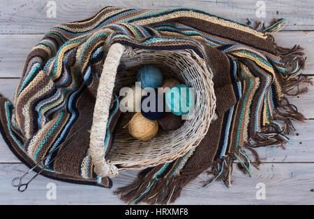 Knitted woolen scarf and yarn balls in a wicker basket on a wooden surface Stock Photo