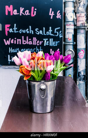 Berlin, Prenzlauer Berg . Pretty tulips in metal ice bucket container on table outside restaurant with menu board Stock Photo