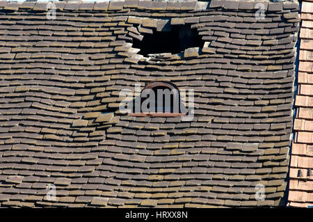 Old damaged tiled roof with broken tiles and a hole on the roof Stock Photo