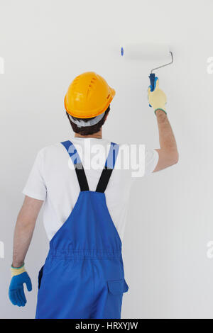 Worker in overalls uniform and hardhat painting the wall with paint roller Stock Photo