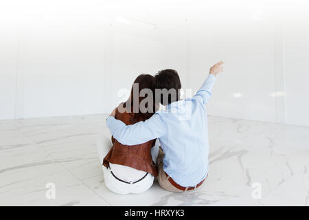 Young couple sitting on the floor of new empty house pointing up into the air Stock Photo