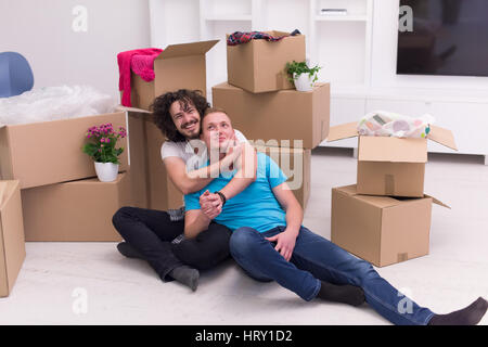 Relaxing in new house. Cheerful young gay couple sitting on the floor while cardboard boxes laying all around them Stock Photo