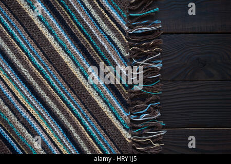Knitted fabric fragment handmade with strips on a dark wooden surface. Background Stock Photo
