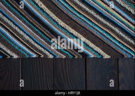 Knitted fabric fragment handmade with strips on a dark wooden surface. Background Stock Photo