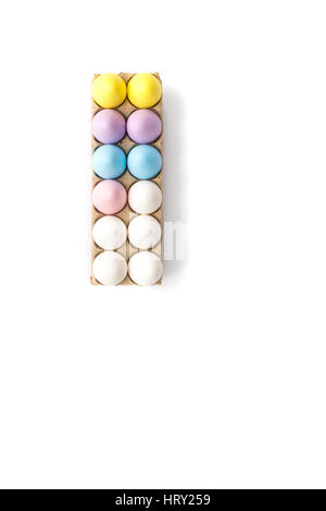 Seven Easter eggs dyed lilac, yellow. blue and pink and five white hen's eggs in a tan cardboard carton from above with white background. Copy space. Stock Photo