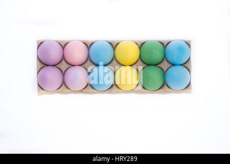A dozen Easter eggs dyed lavender, blue, yellow, pink and green in tan cardboard carton against white background from above with copy space. Stock Photo