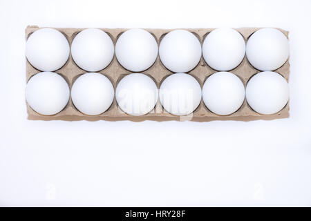 A dozen white hard boiled hen's eggs in a tan cardboard carton against a white background from above with copy space. Stock Photo
