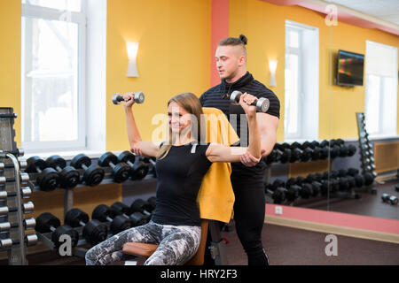 Woman with her personal fitness trainer in the gym exercising power gymnastics with a barbell Stock Photo