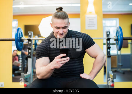 Young handsome man using phone while having exercise break in gym. Stock Photo