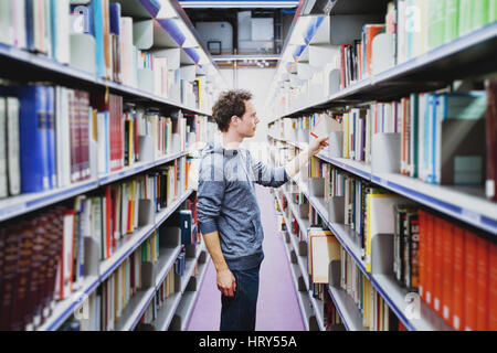 student in the library of university, young caucasian man taking book from bookshelf, education concept Stock Photo