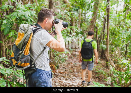 nature photographer in tropical jungle, group of tourists hiking in the forest, man taking photo with big camera Stock Photo